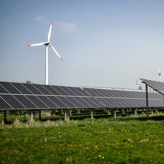 Mehrere Windkraftanlagen stehen hinter einem Solarpark.