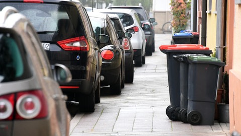 In einer Straße parken Autos auf dem Gehweg, zudem stehen Mülltonen vor einem Haus (Archivbild).