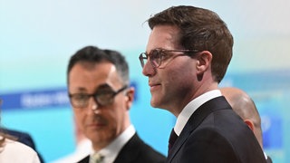 Cem Özdemir und Manuel Hagel stehen in einem Fernsehstudio. Die CDU will Gespräche mit den Grünen aufnehmen.