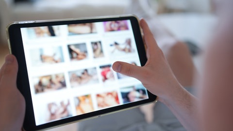 Ein junger Mann schaut sich auf einem Smartphone eine Porno-Internetseite an (gestellte Szene)