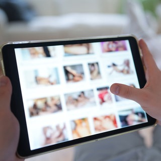 Ein junger Mann schaut sich auf einem Smartphone eine Porno-Internetseite an (gestellte Szene)