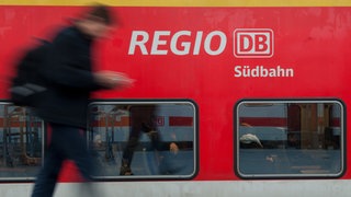 Ein Mann, der nur verschwommen zu sehen ist, läuft an einem Regionalzug der Südbahn entlang. Ein EuGH-Urteil könnte Pendlern höhere Preise bescheren.