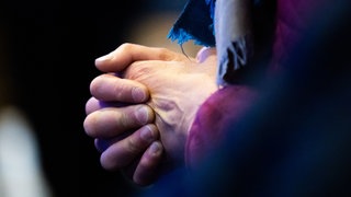 Eine Gläubige faltet die Hände. Die Kirchen in BW rufen an Ostern zu Solidarität mit Leidenden auf.