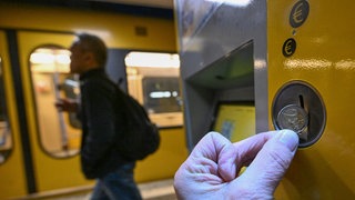 Ein Mann läuft an einem Bahnsteig entlang einer Stadtbahn. Eine Person wirft eine Zwei-Euro-Münze in einen Ticketautomaten. Häufig sind es Armutsbetroffene, die ohne Fahrschein fahren. Das soll laut Bundesjustizministerin Hubig keine Straftat mehr sein. (Symbolfoto)