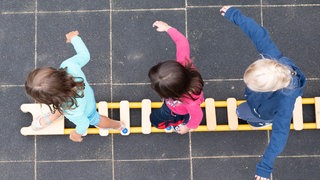Kinder balancieren auf einem Spielplatz über eine liegende Leiter.
