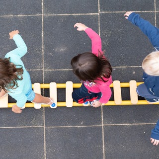 Kinder balancieren auf einem Spielplatz über eine liegende Leiter.