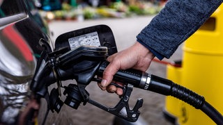 Eine Person hält die Zapfpistole einer Tankstelle in den Sutzen eines schwarzen Autos. Beim Carsharing müssen Fahrer zwar selbst tanken, die Kosten tragen aber die Anbieter.