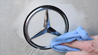 Das Mercedes-Benz Logo auf einem Fahrzeug wird geputzt. Verbände kritisieren den Autobauer für eine hohe Dividendenausschüttung.