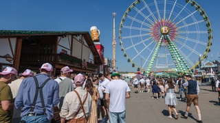 Bei schönem Wetter startet das 86. Stuttgarter Frühlingsfest. Menschen warten vor einem Bierzelt, im Hintergrund steht ein Riesenrad. 