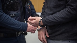 Ein Justizbediensteter löst im Landgericht die Handschellen eines Tatverdächtigen.