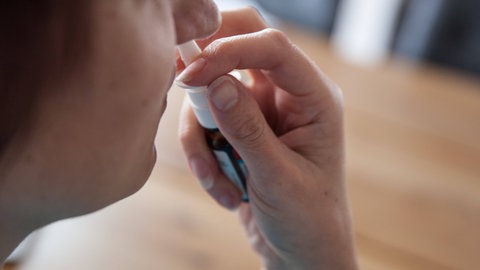 Frau verabreicht Nasenspray gegen Pollenallergie - das Spray hilft bei einer verstopften Nase durch Heuschnupfen.