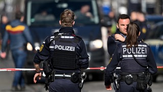 Ein Polizist und eine Polizistin sind von hinten fotografiert, wie sie nach der Amokfahrt in Mannheim die Innenstadt absichern.