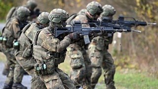 Rekureten der Bundeswehr laufen bei einer Gefechtsausbildung mit gezogenen Gewehren durch ein Waldstück.
