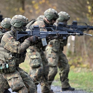 Rekureten der Bundeswehr laufen bei einer Gefechtsausbildung mit gezogenen Gewehren durch ein Waldstück.