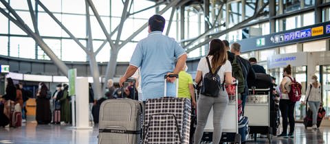 Reisende mit Koffern stehen an den Check-in-Schaltern am Flughafen Stuttgart Schlange.