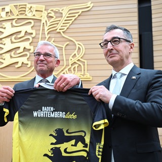 Der neu gewählte Ministerpräsident Cem Özdemir bekommt von Thomas Strobl ein Trikot mit dem Logo des Landes Baden-Württemberg.