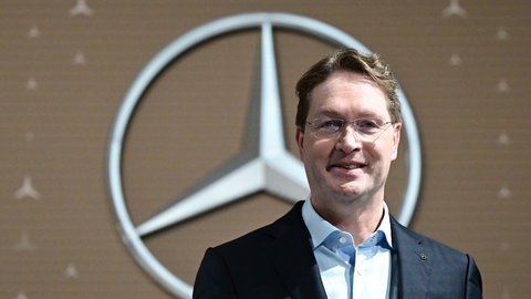 Ola Källenius, Vorstandsvorsitzender der Mercedes-Benz Group AG, steht vor der Bilanz-Pressekonferenz vor einem Mercedes-Benz Markenlogo.