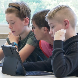 Zwei Schüler üben mit einer Lehrerin lesen