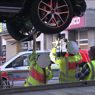 Auto auf einer hzebebühne und Polizizistinnen stehen darunter