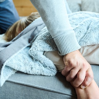 Symbolbild: Eine erwachsene Person greift ein Kind fest am Arm, während es auf einer Couch liegt.