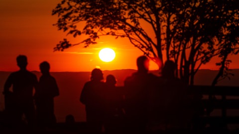 Menschen schauen sich einen Sonnenuntergang an. Die Sommerhitze macht sich in Baden-Württemberg breit. Viele sehnen sich nach einer Möglichkeit zum Abkühlen.