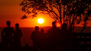 Menschen schauen sich einen Sonnenuntergang an. Die Sommerhitze macht sich in Baden-Württemberg breit. Viele sehnen sich nach einer Möglichkeit zum Abkühlen.