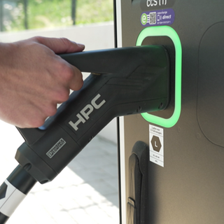 Ein Mann steckt das Kabel eines E-Autos in eine Schnellladesäule.