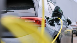 Ein graues E-Auto ist mit einem gelben Kabel zum Aufladen an eine Ladesäule angeschlossen. Durch hohe Verkaufszahlen und bessere Batterien werden gebrauchte Elektroautos immer attraktiver.