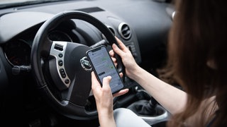 Eine Frau sitzt mit Handy am Steuer.