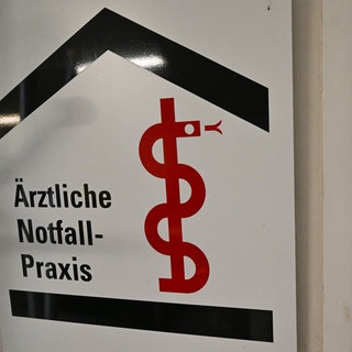 Eine Frau, die nur verschwommen im Hintergrund zu sehen ist, betritt eine Ärztliche Notfall-Praxis.