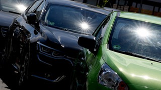Die Sonne reflektiert sich in den Winschutzscheiben parkender Autos. 