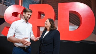 Das junge Duo aus Robin Mesarosch (l) und Isabel Cademartori (r) steht in der Donauhalle vor dem Beginn eines Landesparteitags der SPD Baden-Württemberg vor einem Parteilogo.
