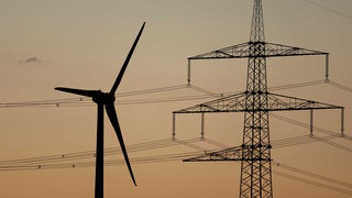 Ein Strommast steht bei Sonnenuntergang vor einem Windrad. Umweltministerin Thekla Walker fordert einen Südbonus bei EEG-Ausschreibungen.