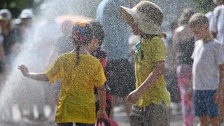 Hitze in Kitas Kinder kühlen sich an einem Wassersprenger ab. 
