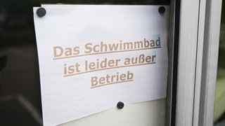 Eine Zettel mit der Aufschrift "Das Schwimmbad ist leider außer Betrieb" hängt vor einem Bad (Archivbild).