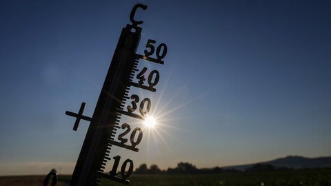 Die Sonne scheint hinter einem Thermometer. In Baden-Württemberg wird es wieder richtig heiß.