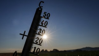 Die Sonne scheint hinter einem Thermometer. In Baden-Württemberg wird es wieder richtig heiß.