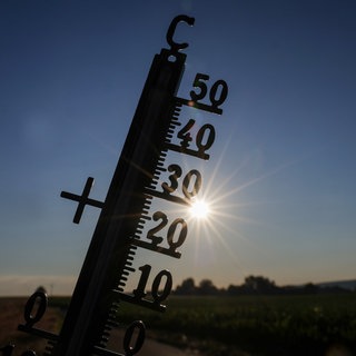 Die Sonne scheint hinter einem Thermometer. In Baden-Württemberg wird es wieder richtig heiß.