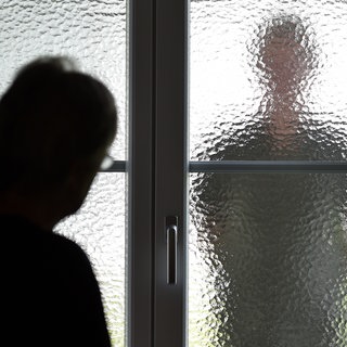 Eine Frau sieht den Schatten eines Mannes hinter einer Glastür. Wie können Stalking-Opfer geschützt werden?