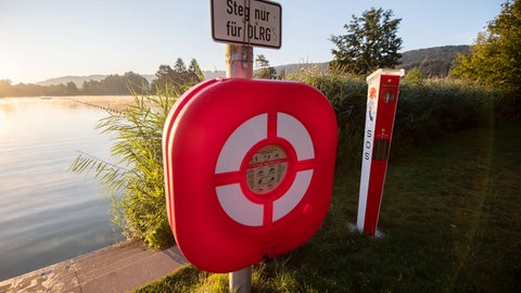 Ein sogenanntes Rettungsmittel mit einem Rettungsring hängt am frühen Morgen am Badesee Plüderhausen an einer Säule.