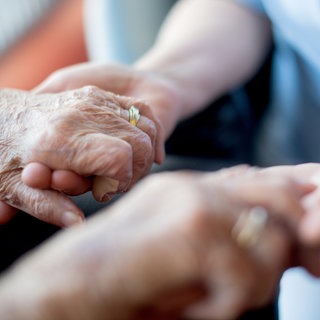Eine Pflegekraft hält einem alten Menschen die Hand.