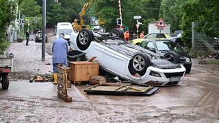 Auf einer Straße in Rudersberg liegt ein durch ein Hochwasser umgestürtztes Auto auf dem Dach. Tagelang kämpften 2024 Einsatzkräfte aus BW und Bayern gegen die Flut und ihre Folgen.