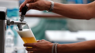 Eine Servicekraft zapft in einer Gaststätte ein Bier.