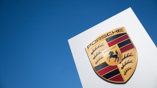 Das Porsche-Logo ist vor der Porsche Sonderwunsch-Manufaktur an einem Schild zu sehen. 