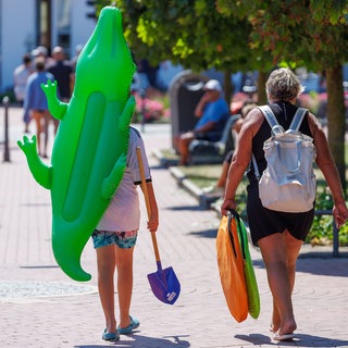 Mit einem aufgeblasenen Krokodil gehen Urlauber über die Strandpromenade. Urlaub ist für viele Menschen Luxus.