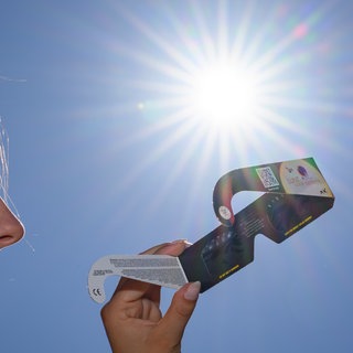 Eine junge Frau setzt sich eine Sonnenfinsternisbrille auf.