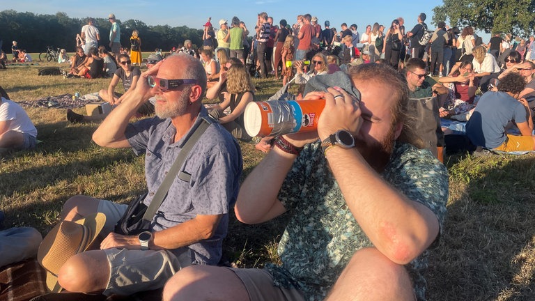 Menschen sitzen auf einem Hügel und warten auf den Beginn der Sonnenfinsternis