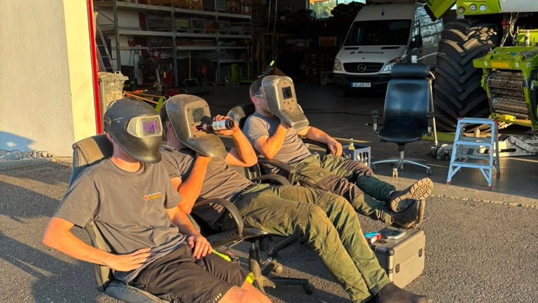 In Schweißermontur schauen drei junge Männer in die Sonne.