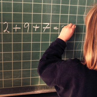 Mädchen schreibt mit linker hand an Tafel. Bis in das späte 20. Jahrhundert war es in Deutschland verbreitet, linkshändige Kinder "auf rechts" umzugewöhnen - Unterstützung für Linkshänder und ihre Besonderheiten fehlte.