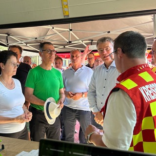 Ministerpräsident Cem Özdemir (Grüne) und Landeswirtschaftsministerin Marion Gentges (CDU) sprechen beim Besuch in Zell am Harmersbach (Ortenaukreis) mit Einsatzkräften der Feuerwehr. Sie stehen dabei in eienem Zelt. Özdemir bedankte sich für den Einsatz der ehrenamtlichen und hauptamtlichen Helferinnen und Helfer.